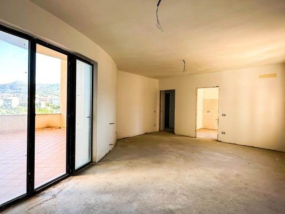 Ampia zona living in costruzione con balcone, finestra e vista panoramica, pronta per arredare; interno di una casa in fase di ristrutturazione in Italia.