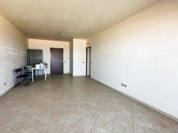 Ampio soggiorno in fase di ristrutturazione con pareti bianche e pavimento in ceramica, pronto per personalizzare la propria casa. Inserisci mobili e arredi per un ambiente accogliente.