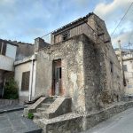 Vecchio edificio in pietra con balcone in ferro e scale in ciottolato, situato in zona residenziale. Struttura storica da ristrutturare, perfetta per investimenti immobiliari o case antiche con charme.