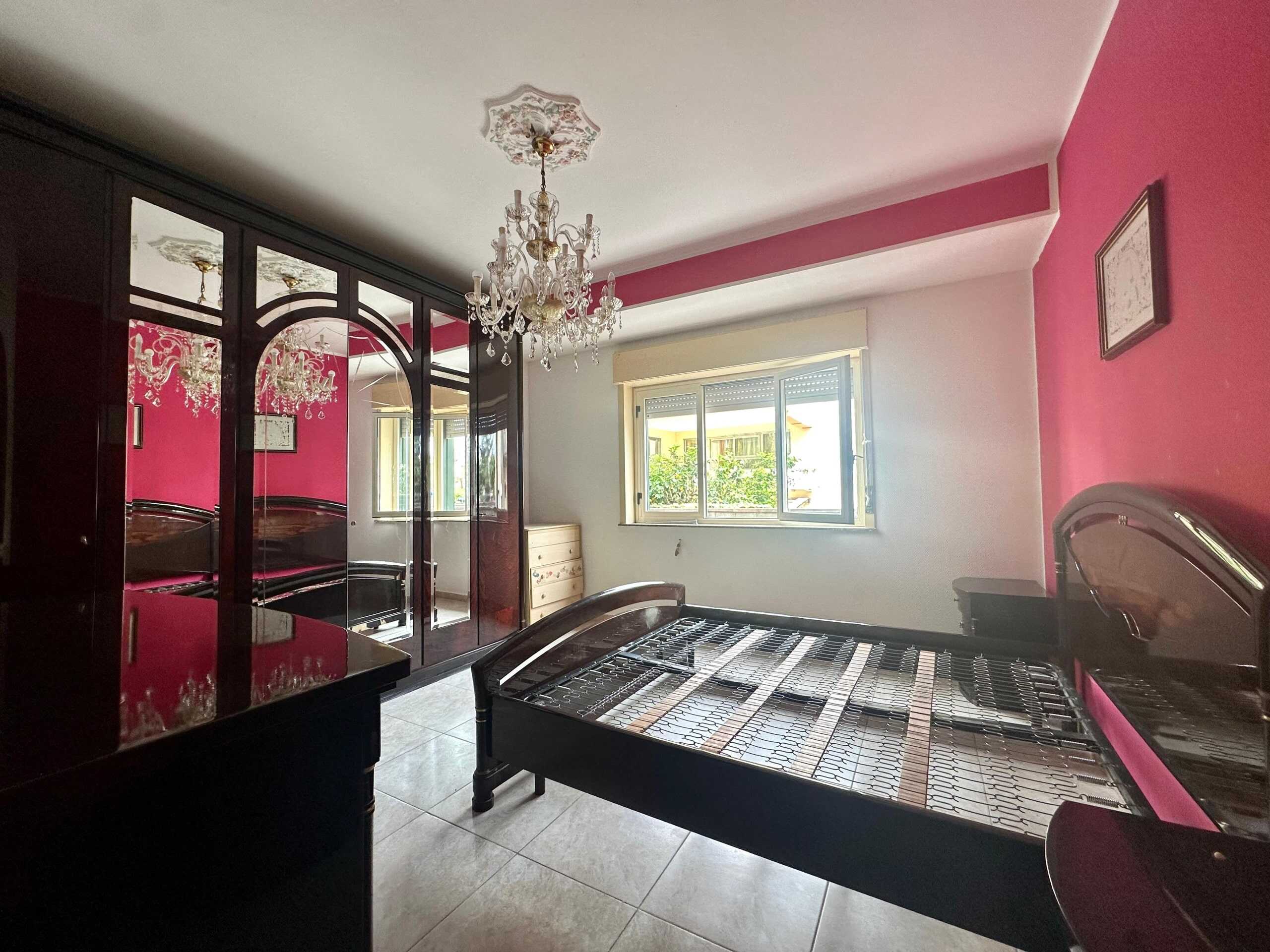 Armadio a specchio, camera da letto con letto senza materasso, pareti rosa, finestra luminosa, arredamento elegante, stile classico moderno, NextCasa, immobile in vendita o affitto in Italia.