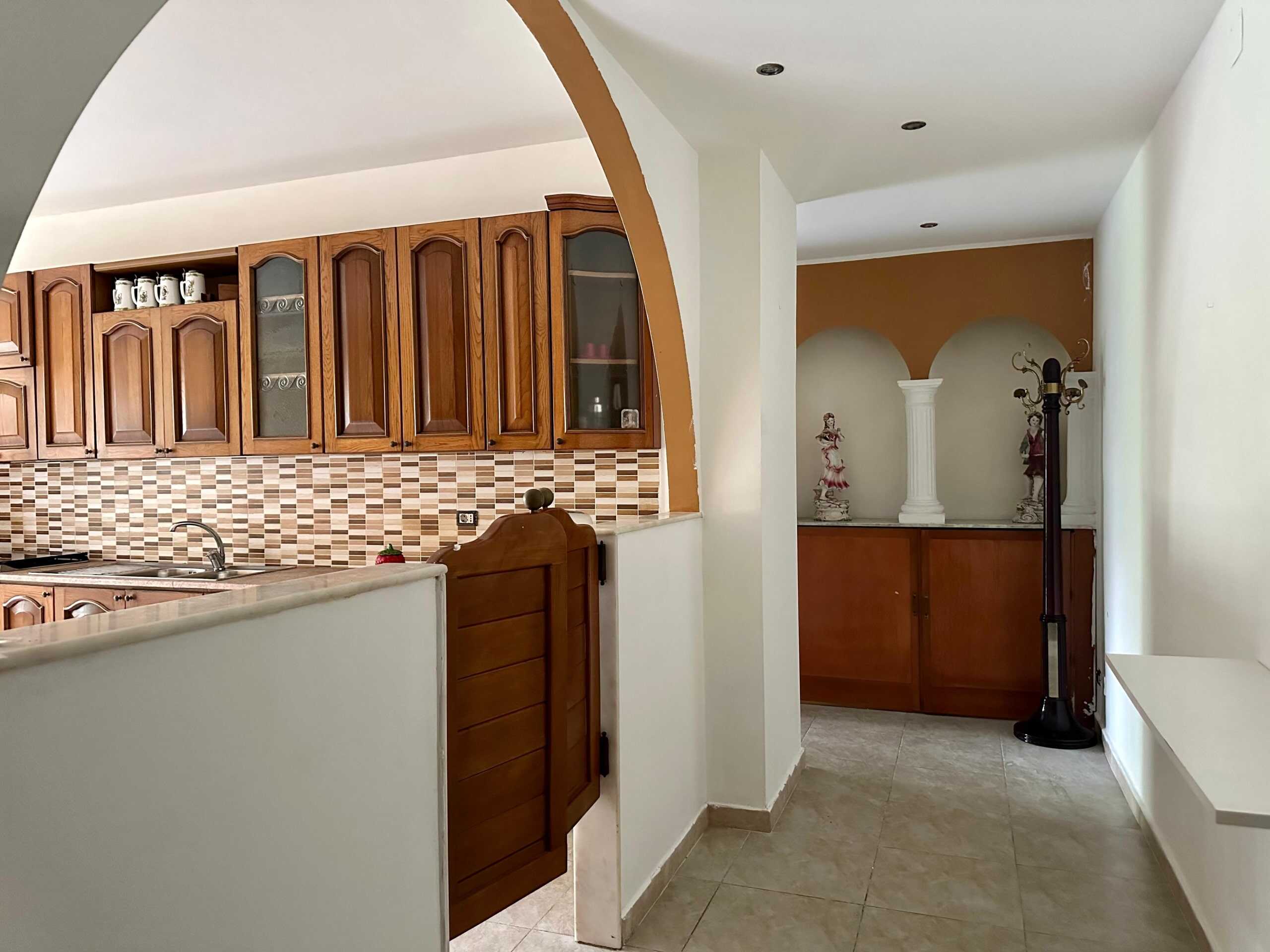 Arco in muratura che divide la cucina e il soggiorno con mobili in legno, decori classici e colonnina decorativa, atmosfera accogliente e elegante in stile tradizionale italiano.