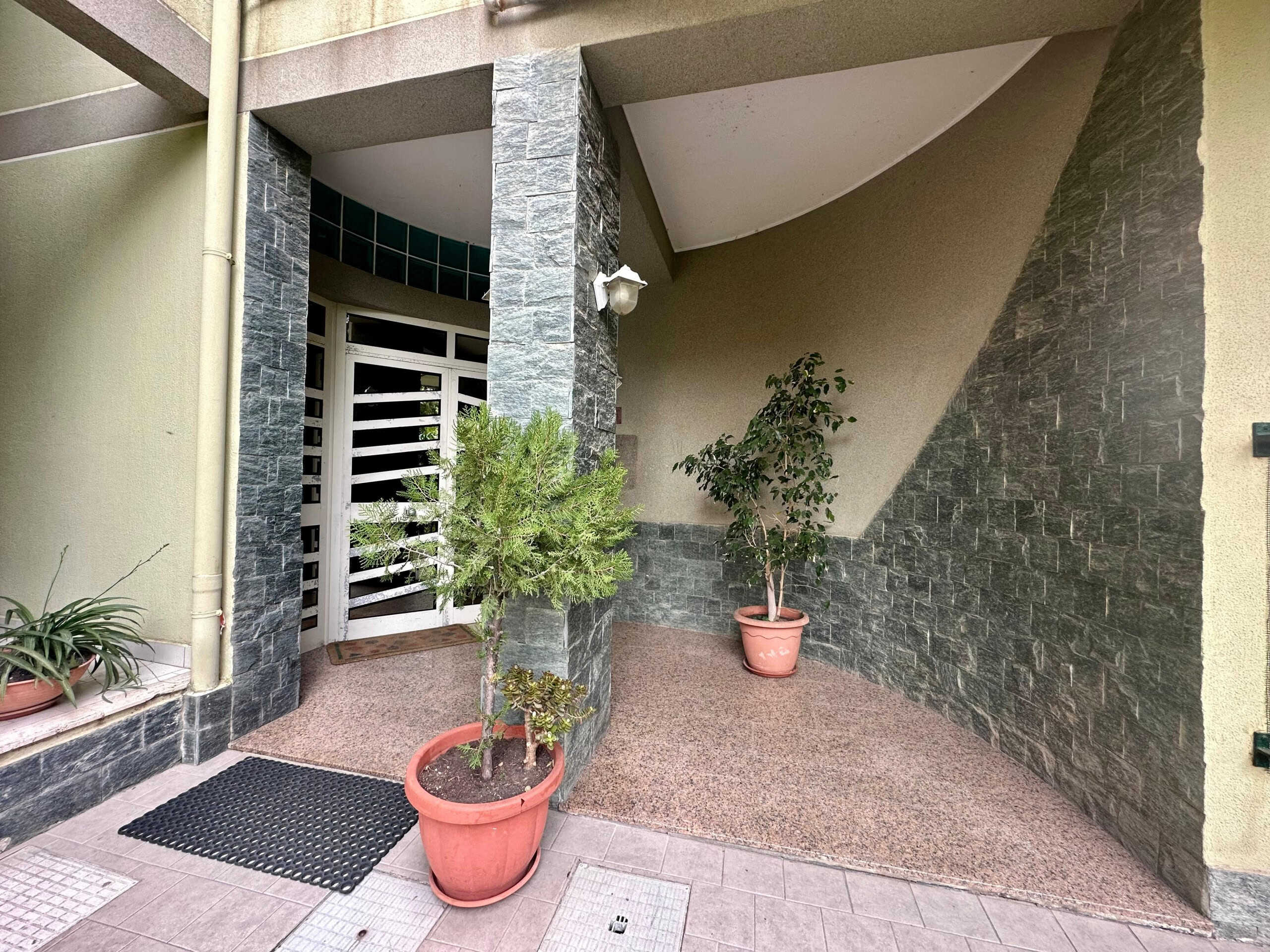Piante in vasi sulla veranda di un ingresso di un appartamento situato in una zona urbana. Esterno di casa con dettagli di architettura moderna, pietre e recinzione in metallo, ideale per servizi immobiliari NextCasa.