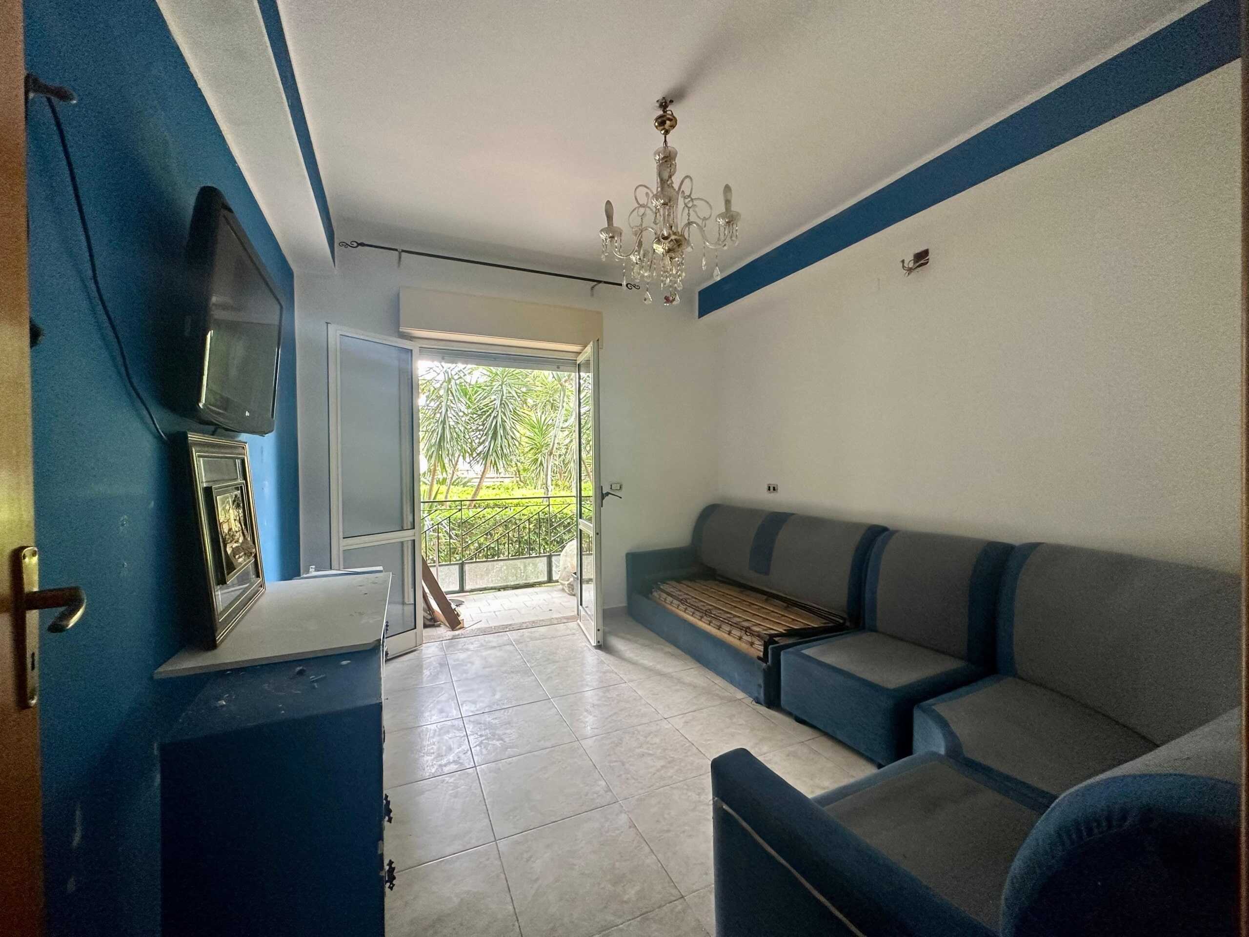 Elegante soggiorno con divano angolare e accesso a balcone, decorato con dettagli blu, ideale per affitti e compravendite immobiliari a NextCasa.