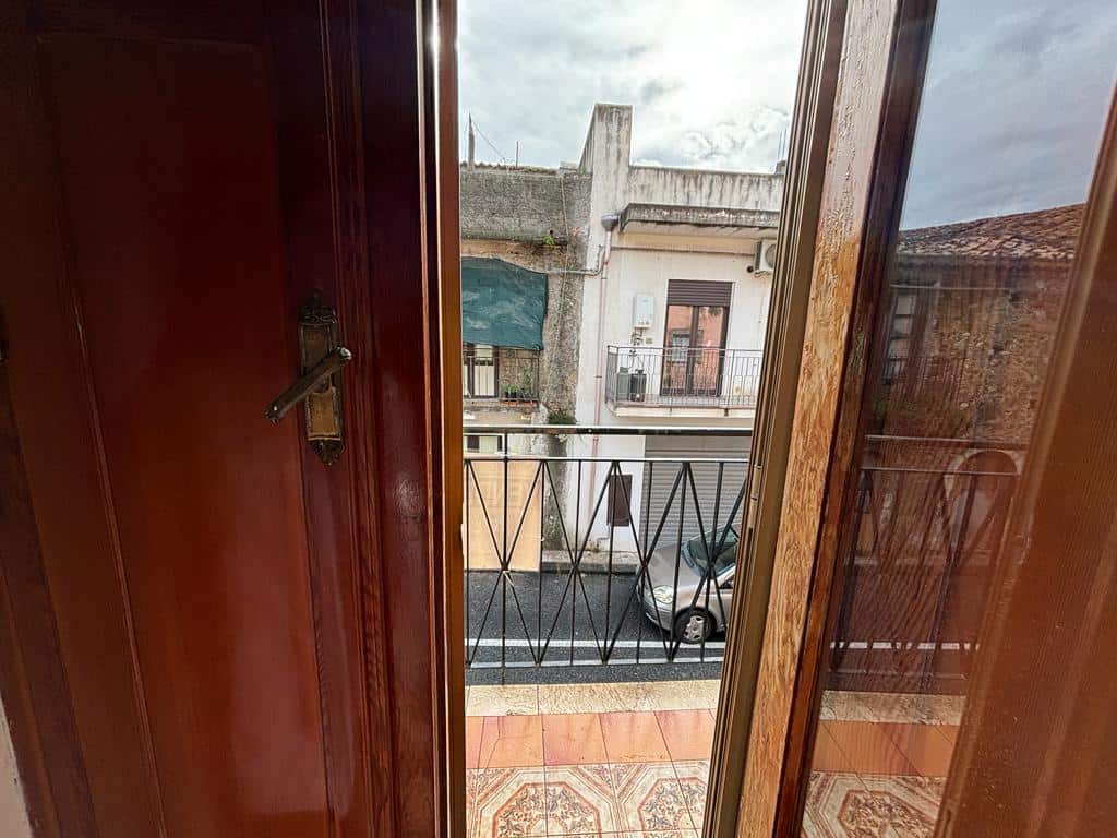 Finestra con vista sulla strada e sui balconi di edifici residenziali, illuminate dalla luce naturale, in un ambiente con rivestimento in legno e pavimento decorato in ceramica.
