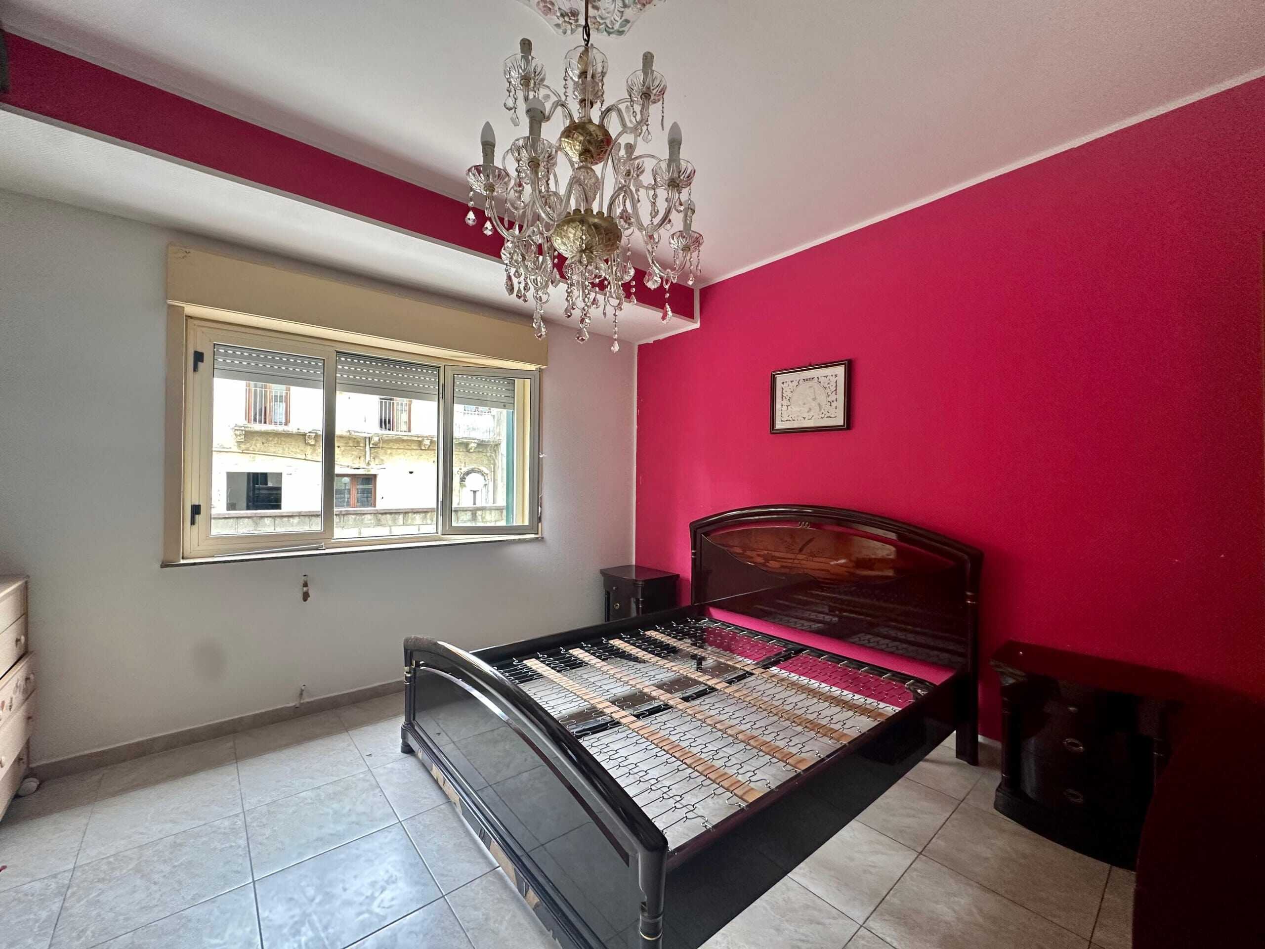 Letto matrimoniale senza rete in camera da letto con parete rosa e lampadario chandelier classico.