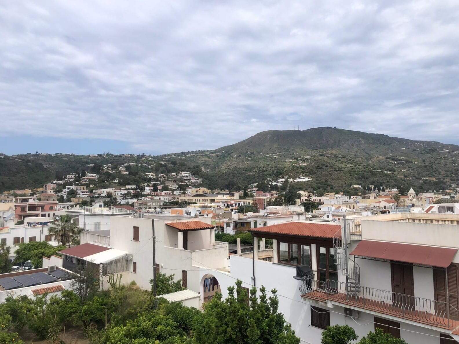 Vista panoramica sulle case di Punta d'Aglio con colline verdi e cielo nuvoloso, ideale per promuovere immobili residenziali in vendita o affitto a Napoli.