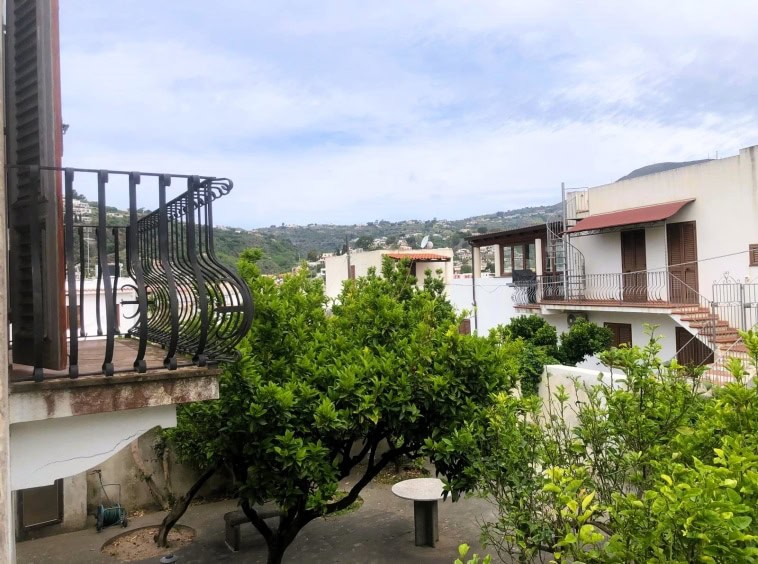 Balcone con ringhiera in ferro battuto, vista su case e colline, verdeggianti giardini e cielo con nuvole, in un appartamento a NextCasa, affaccio su zona residenziale, ambiente luminoso e tranquillo.