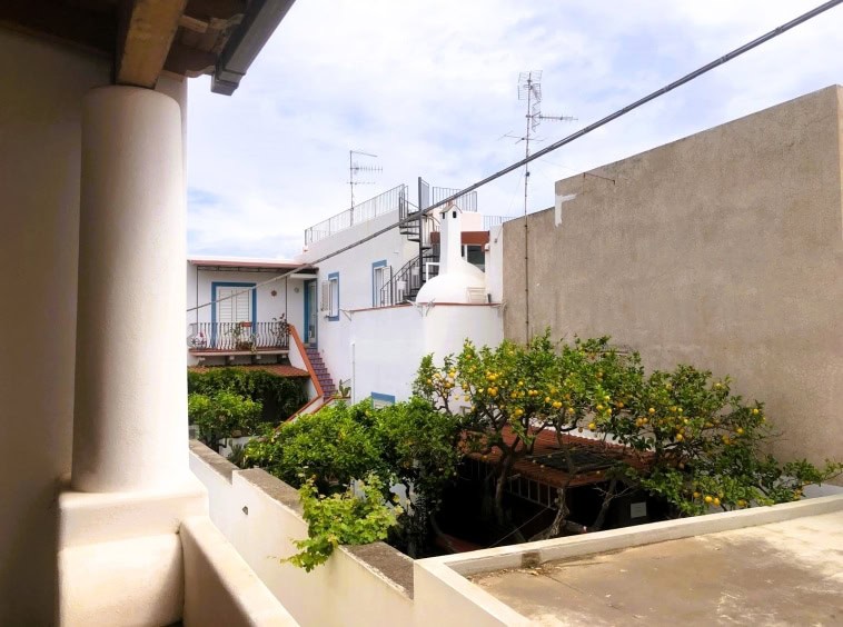 Balcone con vista su case tradizionali siciliane, arance in vaso e tetto in stile mediterraneo, rappresentativo di immobili in vendita a Trapani.