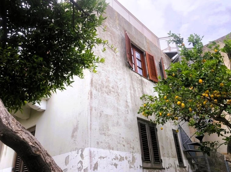 Vecchio edificio con finestra a persiana in legno, pareti in pietra, fontana e limoni in un cortile esterno, fronte strada, atmosfera mediterranea, stile tradizionale italiano.