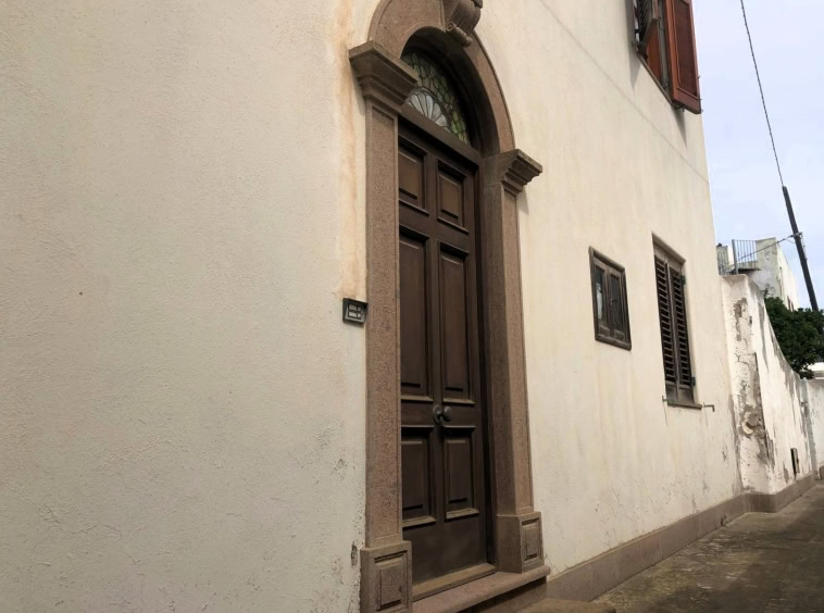 Porta in legno scuro con cornice in pietra, facciata di casa storica, porta principale in stile classico, ingresso elegante, porta d'ingresso con dettagli in pietra, zona residenziale storica Italia.