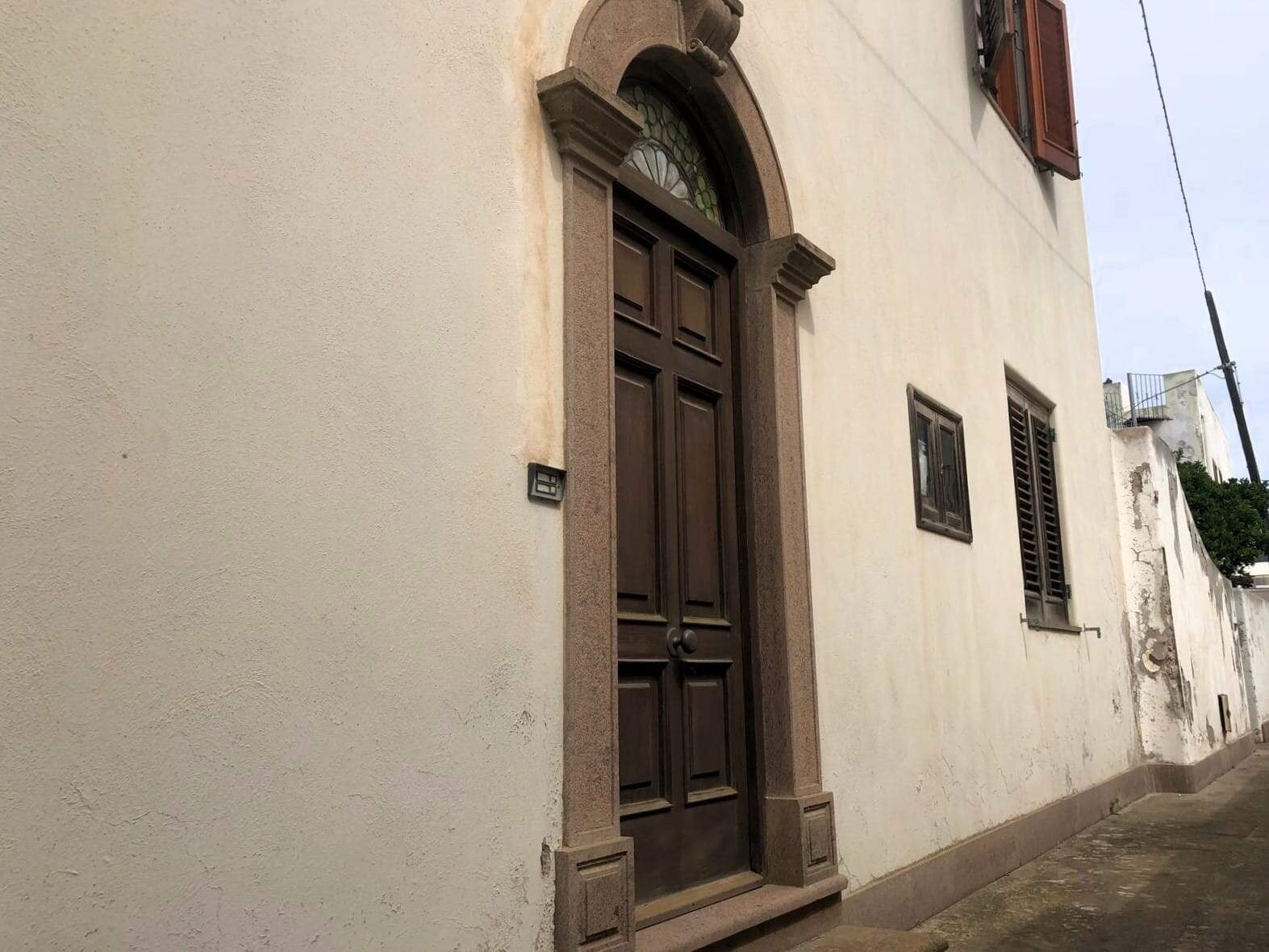 Porta in legno scuro con cornice in pietra, facciata di casa storica, porta principale in stile classico, ingresso elegante, porta d'ingresso con dettagli in pietra, zona residenziale storica Italia.