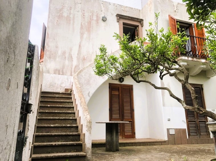 Scala esterna di una casa elegante con elementi in pietra e legno, circondata da piante verdi, ideale per valorizzare immobili storici e di charme in contesti residenziali di pregio.