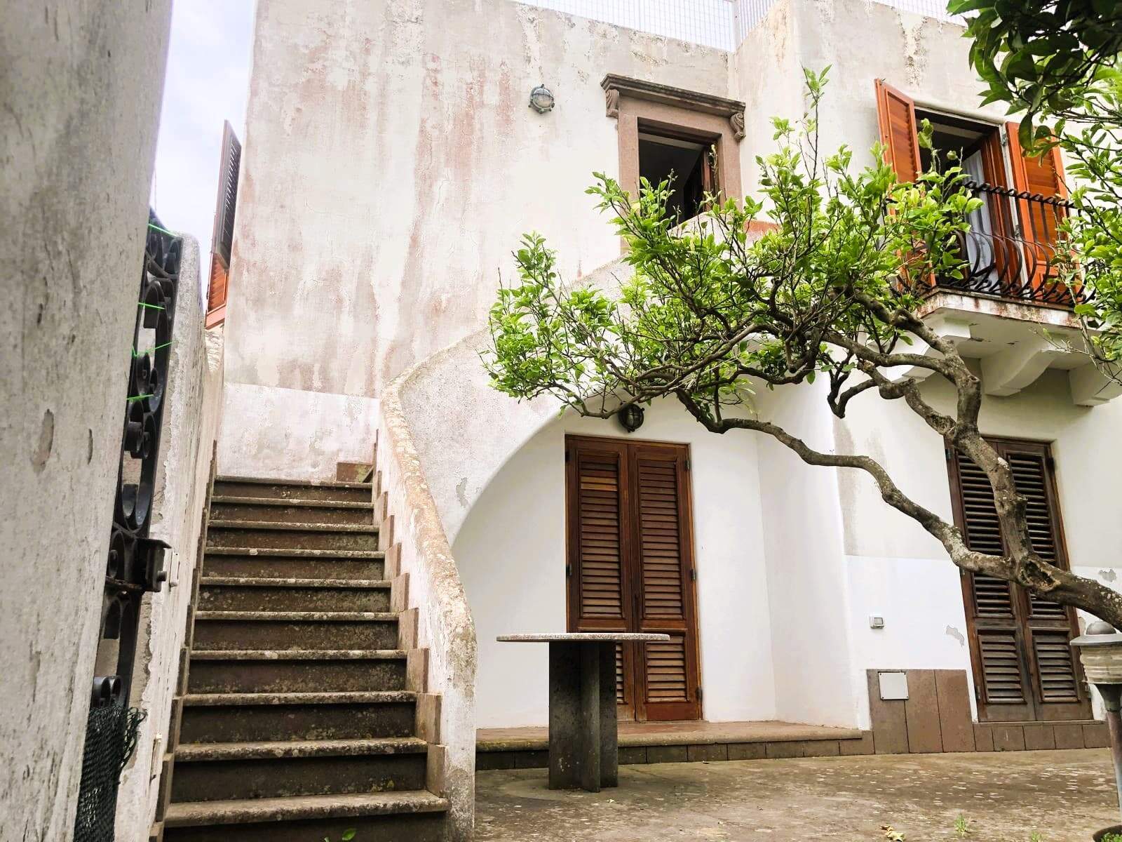 Scala esterna di una casa elegante con elementi in pietra e legno, circondata da piante verdi, ideale per valorizzare immobili storici e di charme in contesti residenziali di pregio.