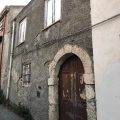 Vecchio edificio in pietra con porta in legno e finestre senza vetri, stile rustico e decadente, suggestivo esempio di architettura storica italiana.