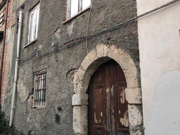 Vecchio edificio in pietra con porta in legno e finestre senza vetri, stile rustico e decadente, suggestivo esempio di architettura storica italiana.