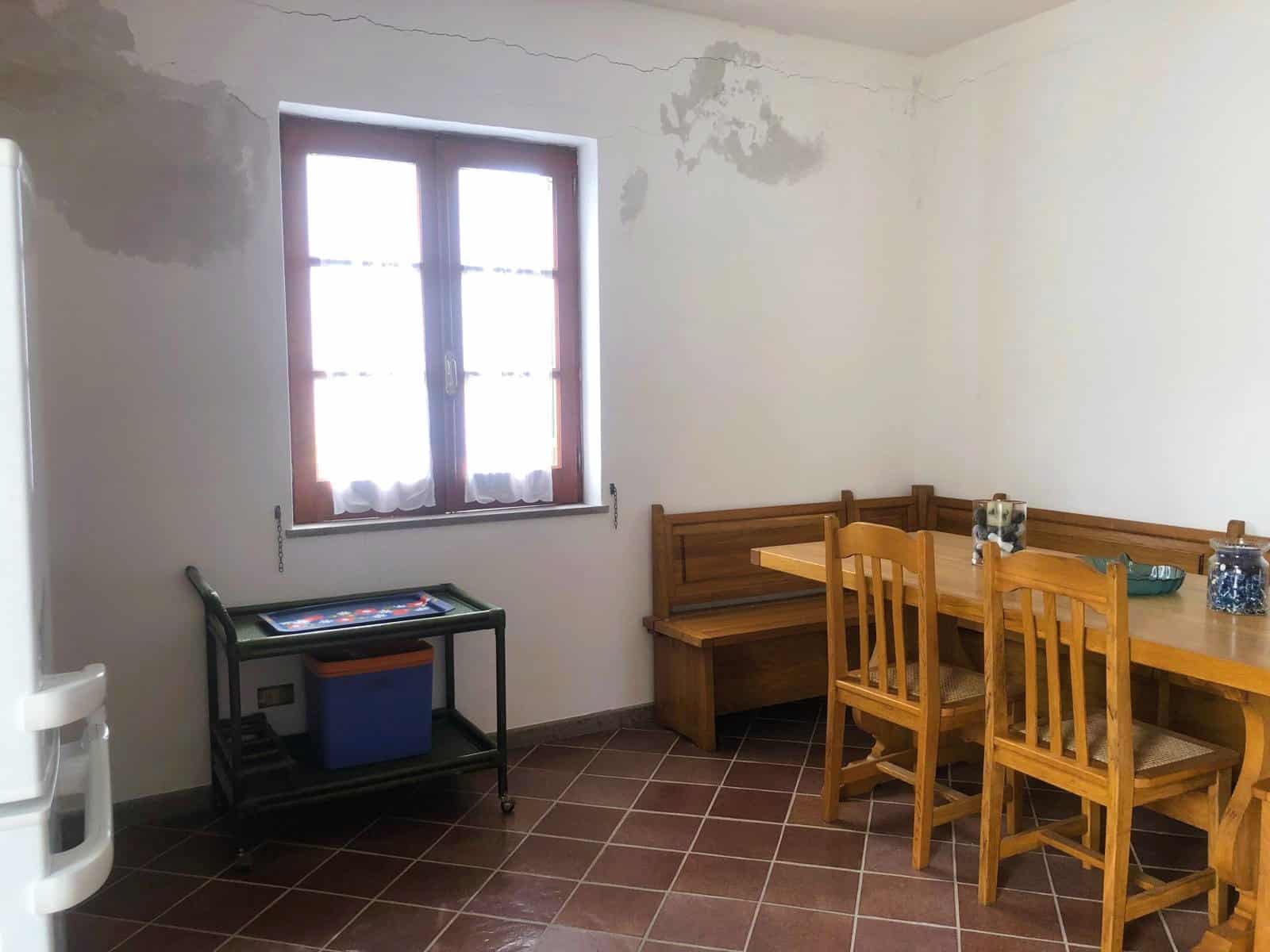 Soggiorno con camino, tavolo in legno e sedie in stile rustico, illuminato da una grande finestra, ambiente caldo e accogliente.