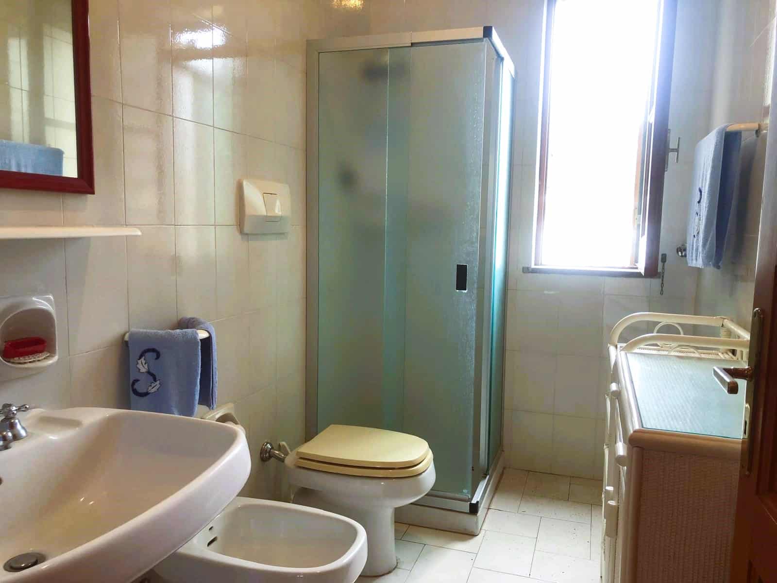 Lavabo, bidet e sanitari in bagno con doccia e finestra aperta, arredo bagno con asciugamani e oggetti bagno, ambiente luminoso e funzionale, NextCasa.