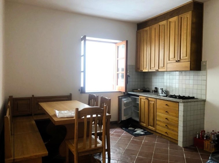 Arredamento cucina rustica con mobili in legno, tavolo con sedie e cucina funzionale in stile tradizionale, ambiente luminoso e accogliente, ideale per affitto case vacanza o residenziali.