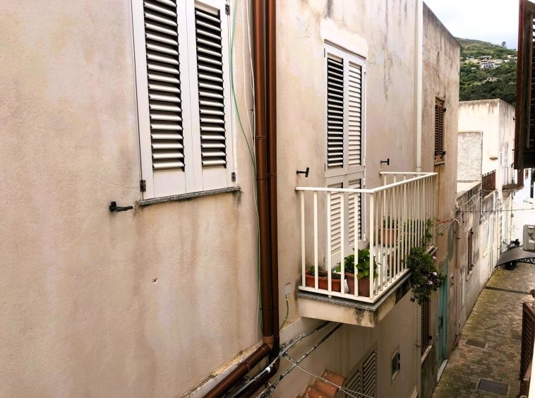 Vicinanze di appartamenti con finestre con persiane in legno, balcone con piante e vista su vicoli di un quartiere storico.