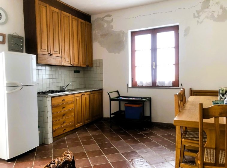 Finestra in cucina con arredamento in legno, angolo pranzo e elettrodomestici in un appartamento rustico ristrutturato.