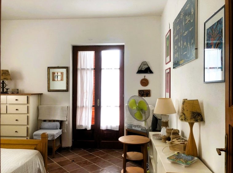Finestra con tende in una stanza spaziosa con arredi in stile rustico, decorazioni alle pareti e illuminazione calda, ideale per ambienti di case vacanze o appartamenti accoglienti.