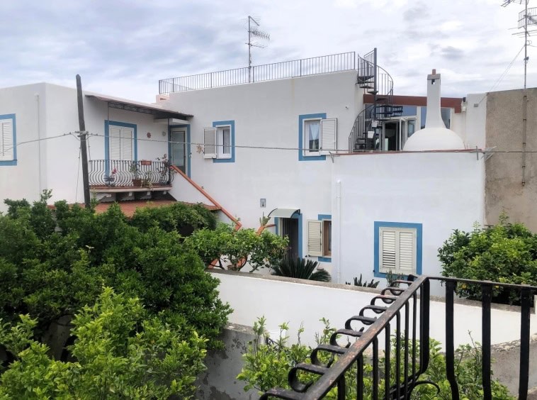 Casale tradizionale alto con tetto piatto e balcone, cuore di Leuca, Puglia, con ampio giardino e vista panoramica sulla zona residenziale.