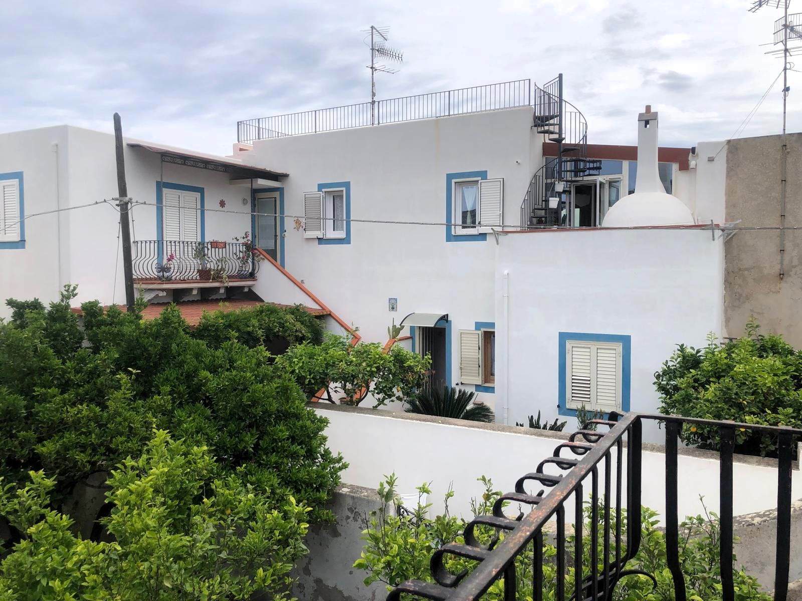 Casale tradizionale alto con tetto piatto e balcone, cuore di Leuca, Puglia, con ampio giardino e vista panoramica sulla zona residenziale.
