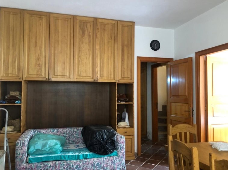 Armadio in legno caldo in soggiorno, con divano con cuscino, spazio di archiviazione e porta in legno che conduce ad una stanza. Atmosfera accogliente, luminosità naturale e dettagli rustici in stile tradizionale.