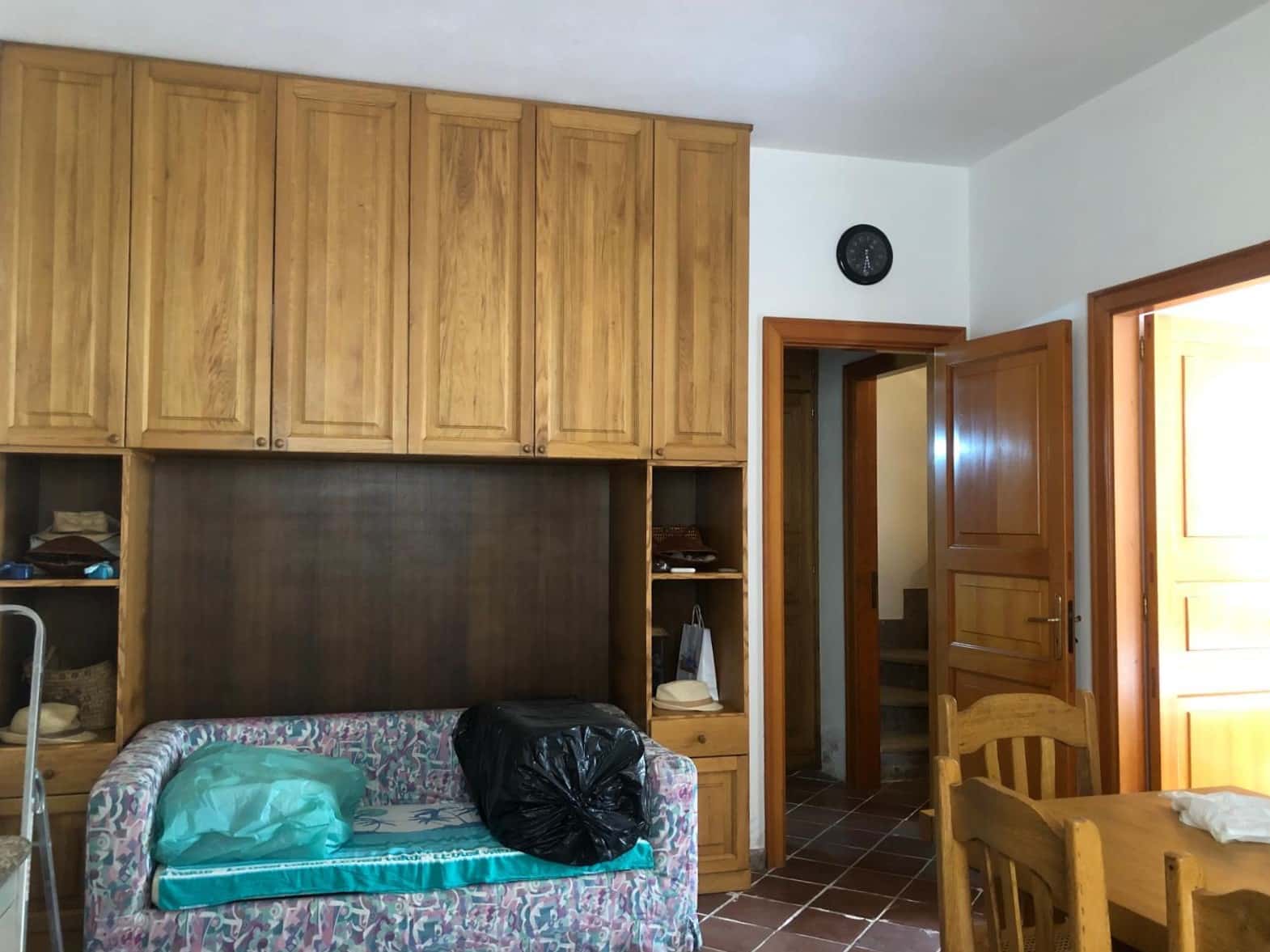 Armadio in legno caldo in soggiorno, con divano con cuscino, spazio di archiviazione e porta in legno che conduce ad una stanza. Atmosfera accogliente, luminosità naturale e dettagli rustici in stile tradizionale.