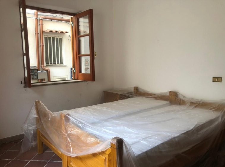 Spazio camera da letto con finestra aperta, pareti bianche e arredamento in legno. La stanza è pronta per essere personalizzata o arredata con mobili e decorazioni. Ideale per proprietà residenziali in vendita o affitto.