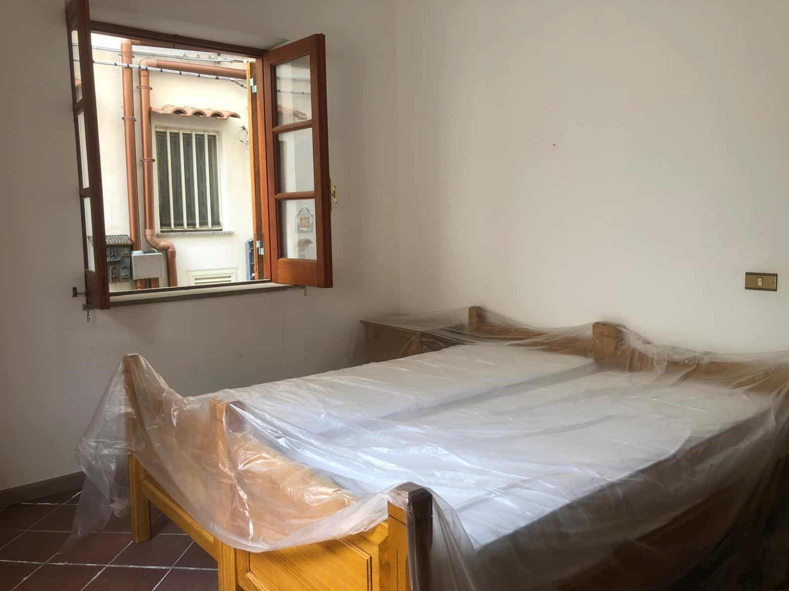 Spazio camera da letto con finestra aperta, pareti bianche e arredamento in legno. La stanza è pronta per essere personalizzata o arredata con mobili e decorazioni. Ideale per proprietà residenziali in vendita o affitto.