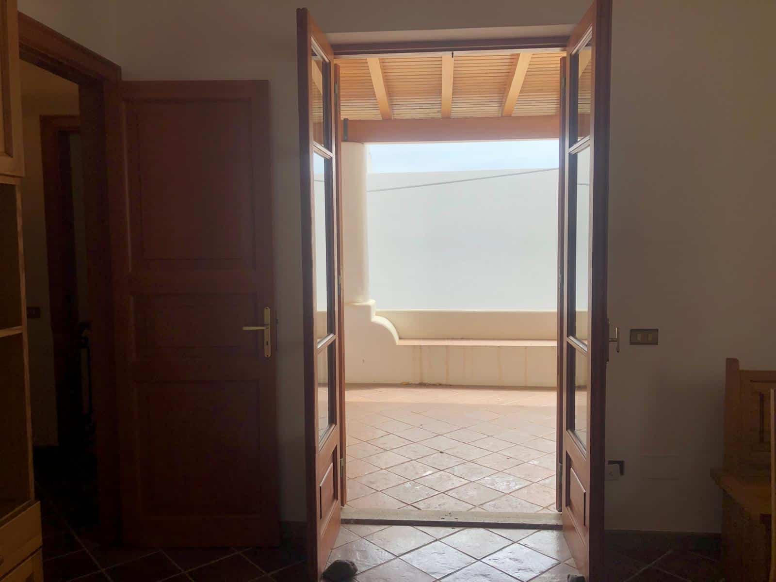 Porta d'ingresso in legno che si apre su un balcone esterno con vetrate, illuminato dalla luce naturale in un ambiente residenziale.