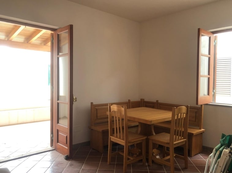 Ventola di vetro e legno con porte battenti aperte che affacciano su una terrazza esterna, arredo cucina rustico in legno chiaro, illuminata da luce naturale, perfetta per ambienti di case vacanza NextCasa.