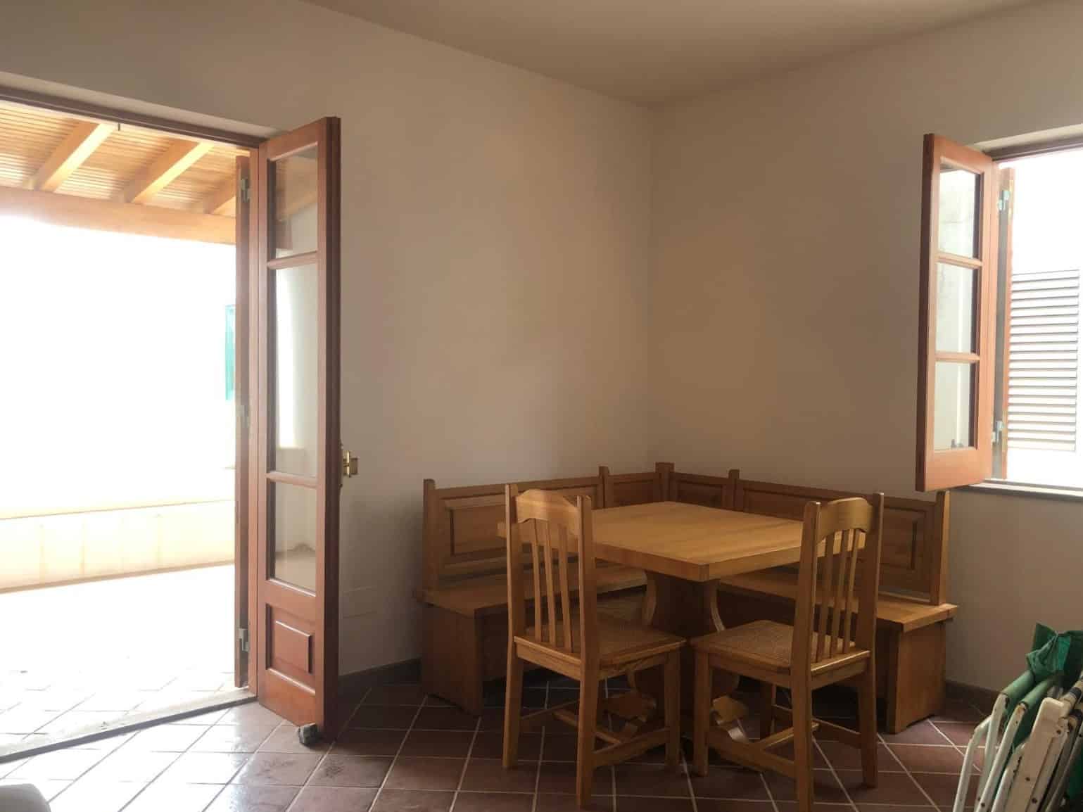 Ventola di vetro e legno con porte battenti aperte che affacciano su una terrazza esterna, arredo cucina rustico in legno chiaro, illuminata da luce naturale, perfetta per ambienti di case vacanza NextCasa.