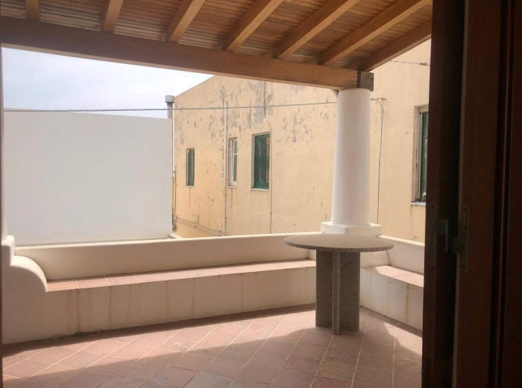 Balcone con vista su edifici storico, pareti in stucco di colore crema, pavimento in piastrelle terracotta e struttura in legno, perfetto per relax e vita all'aperto.