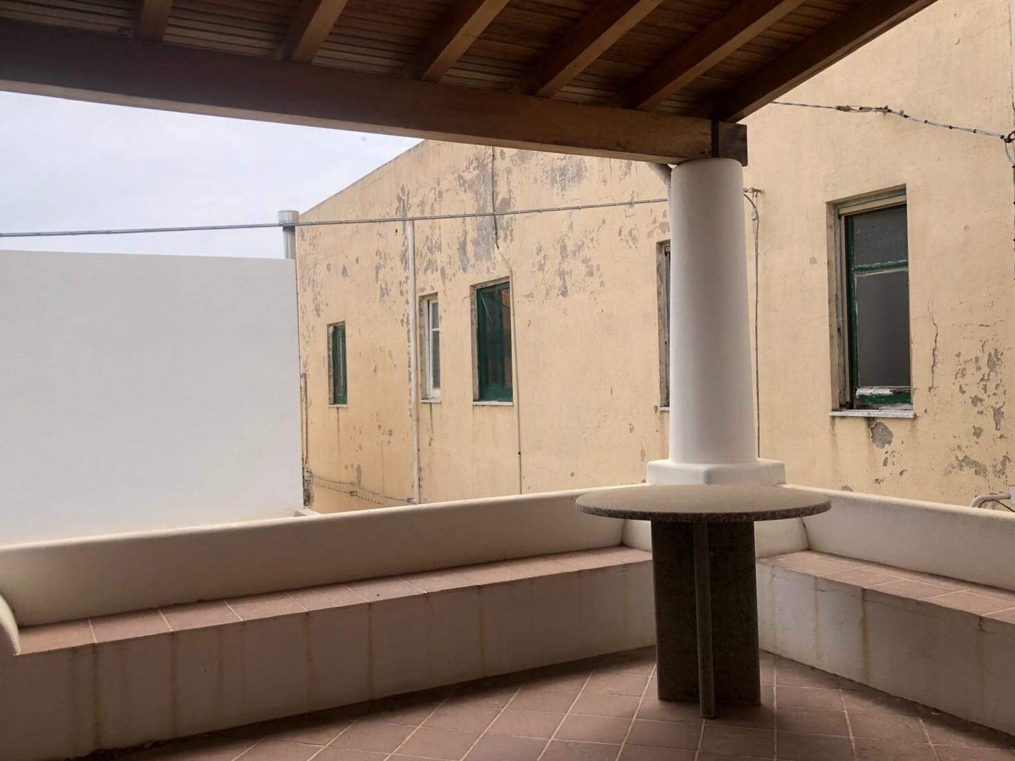 Balcone con vista su edificio storico con finestre, spazio esterno con seduta in muratura e colonnina, ideale per relax e godersi l'ambiente urbano in contesto residenziale.