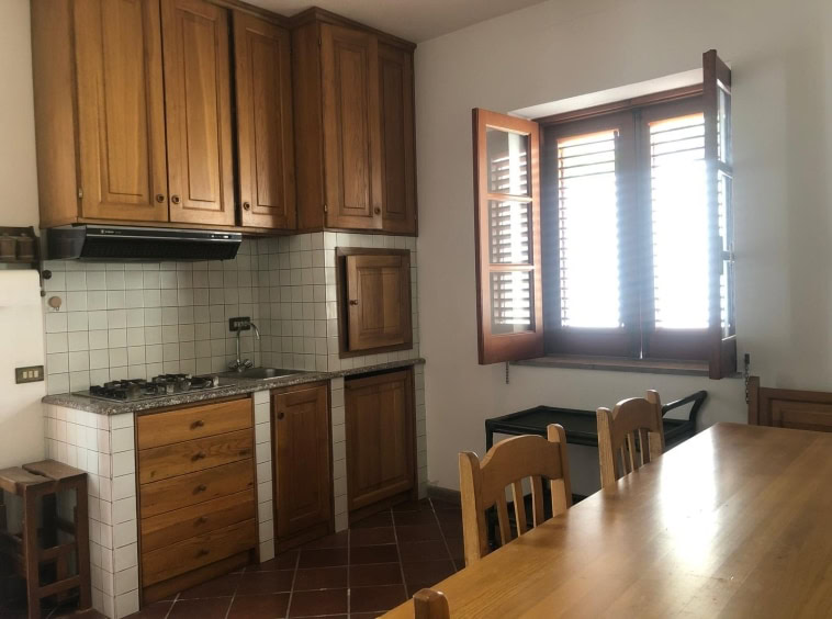 Finestra in cucina con ante in legno, mobili spaziosi, zona pranzo con tavolo e sedie, ambiente luminoso e accogliente, ideale per vivere in ambienti tradizionali e funzionali.
