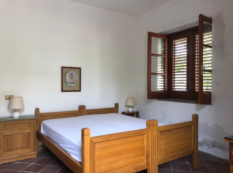 Letto matrimoniale in camera con pareti bianche e finestra con ante di legno, arredamento rustico, stile country, illuminazione naturale, atmosfera accogliente, case vacanza, affitti turistici, NextCasa.