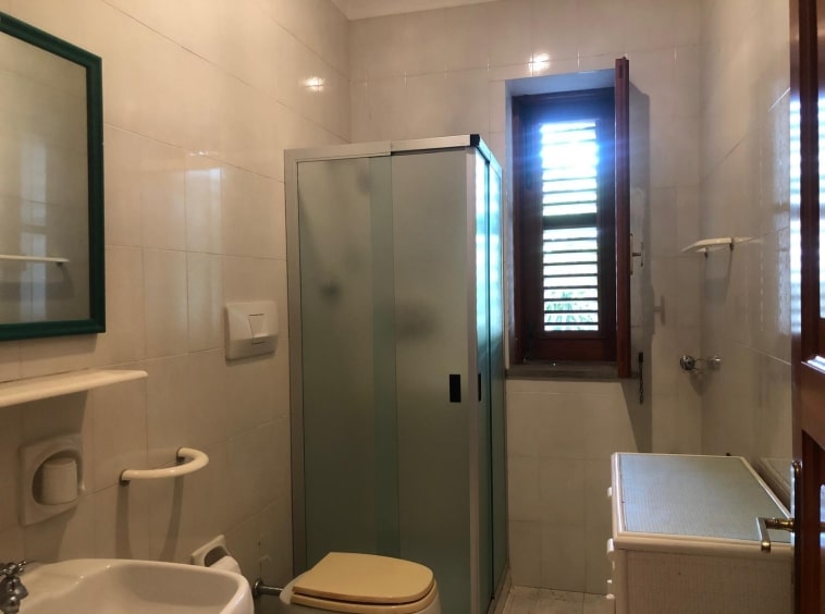Bagno con finestra, sanitari, piastrelle chiare, doccia, armadietto, arredamento semplice, luce naturale, stile classico, bagno funzionale, ambiente luminoso.