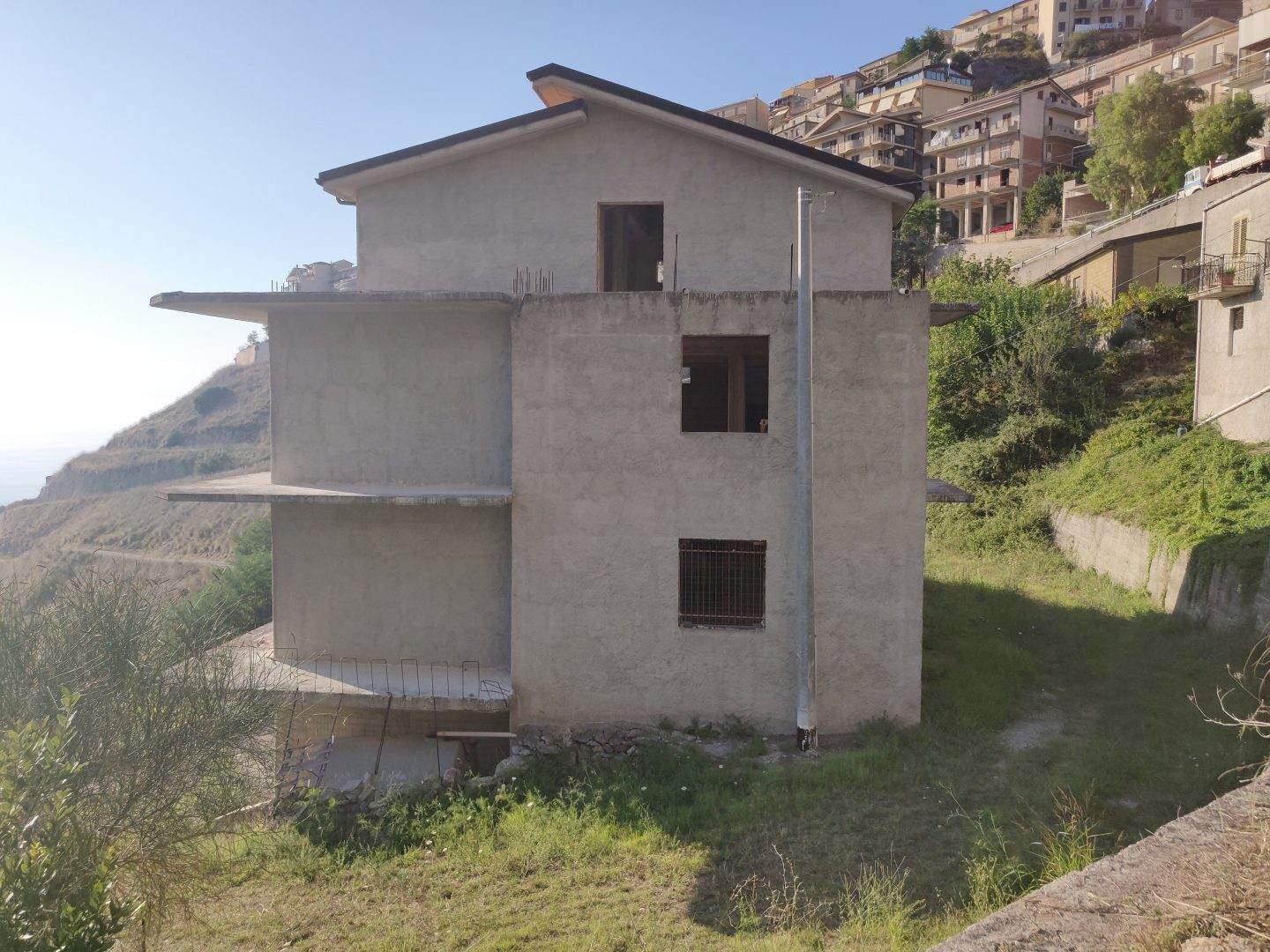 Edificio in fase di costruzione su una collina con vista mare, struttura moderna in cemento, in fase di completamento, situato in zona panoramica con altri immobili residenziali circostanti.