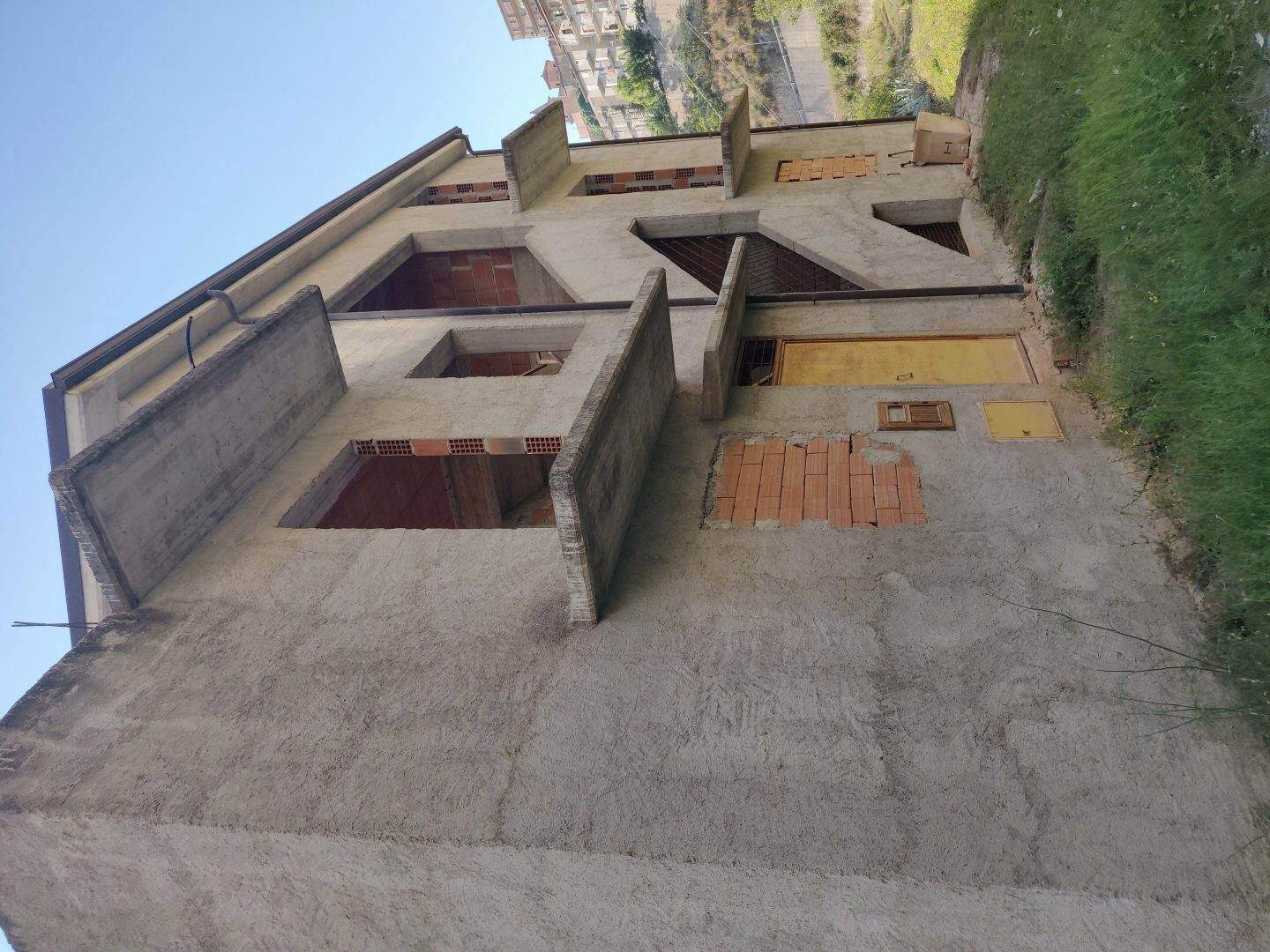 Edificio in fase di costruzione con struttura in cemento e muri in parte in mattoni, pronto per essere rifinito, in un'area verde con vista sulla città.