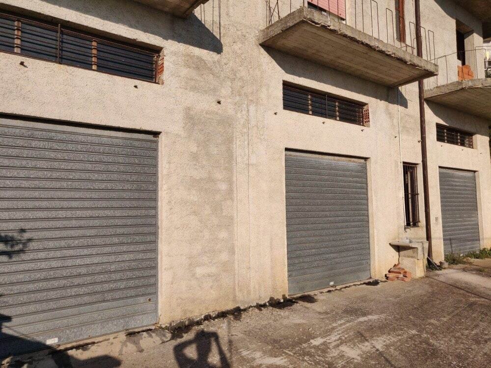 Magazzini con saracinesche in una zona industriale, edificio incompleto con lavori di costruzione in corso, facciata in cemento grezzo e balconi in fase di finitura.