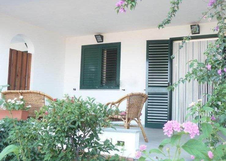 Vista di un terrazzo esterno con sedie in rattan e piante rampicanti fiorite, ambiente accogliente e tranquillo, ideale per relax e momenti di convivialità.