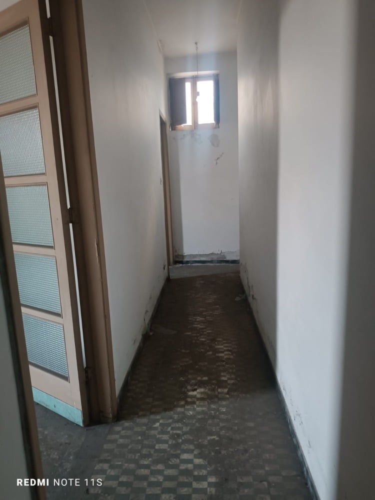Corridor di una proprietà in fase di ristrutturazione, pareti bianche, pavimento in piastrelle vintage, luce naturale da piccola finestra, ambiente ideale per interventi di ristrutturazione casa.