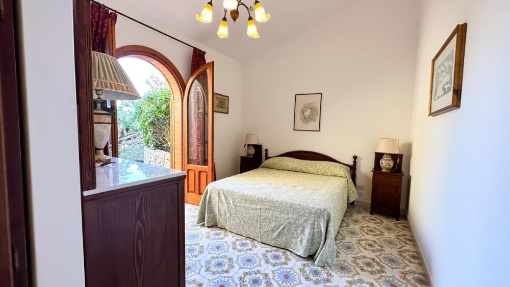 Camera da letto matrimoniale con arredi classici e accessori vintage, illuminata da luce naturale attraverso la porta finestra in legno, perfetta per affitti turistici di charme.