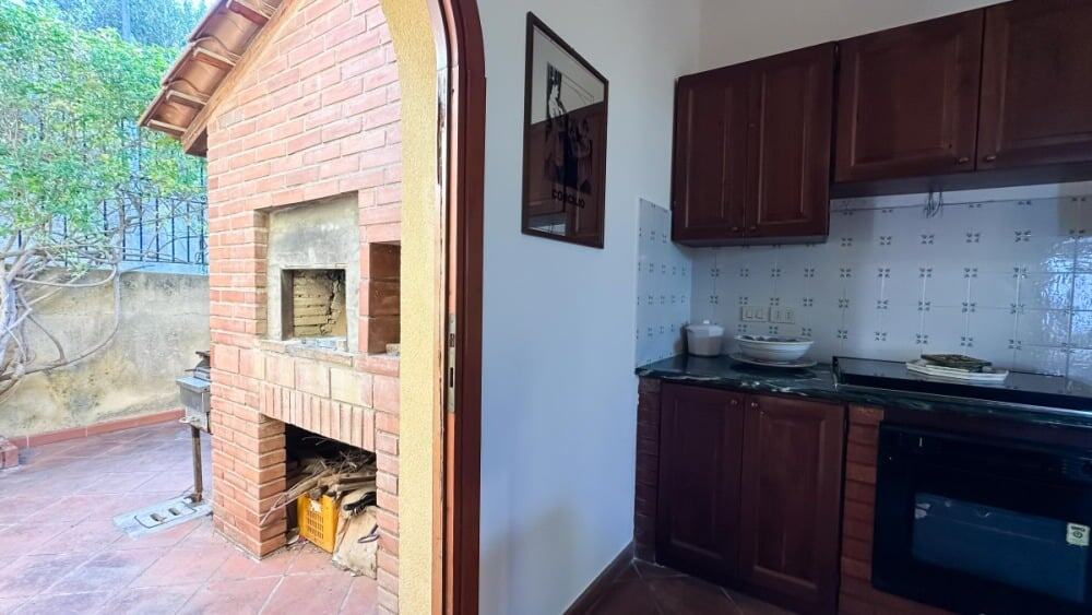 Finestra che mostra un'area esterna con barbecue in mattoni e zona terrazzo, ideale per spazi outdoor e attività di cucina all'aperto.