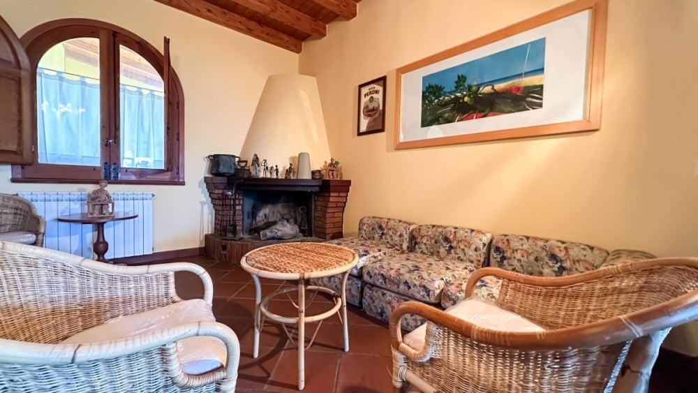 Accogliente soggiorno con camino in stile rustico, arredamento in vimini e affreschi alle pareti, perfetto per un ambiente familiare e rilassante.