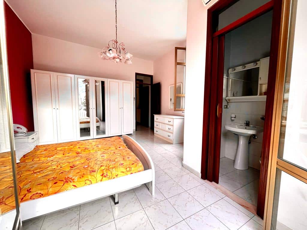 Armadio guardaroba bianco con specchi e camera da letto con letto doppio, fiorellini e copriletto arancione.