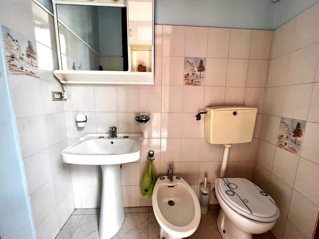 Bagno elegante con lavabo, bidet e toilette in stile classico, rivestimenti ceramici decorati e specchio frontale, ideale per ambienti di case in vendita o affitto.
