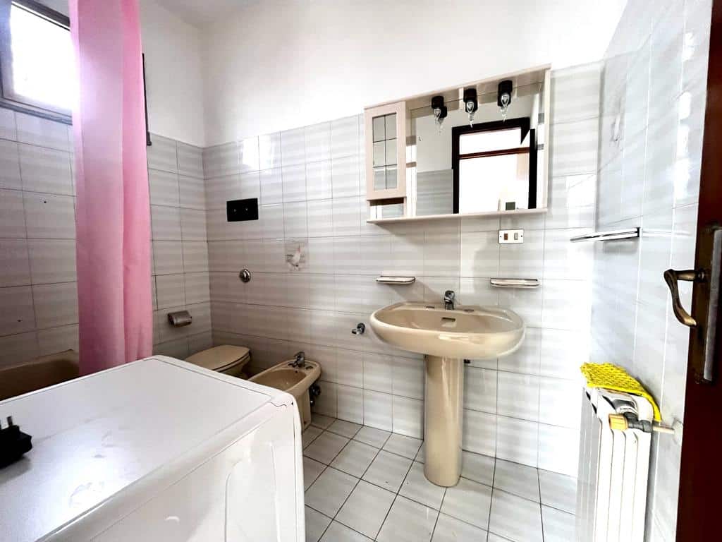 Lavanderia e bagno con lavabo, wc, bidet in ambiente luminoso con piastrelle chiare, finestra, specchio e mobili bagno sospesi, ideale per ristrutturazioni o abitazioni moderne.